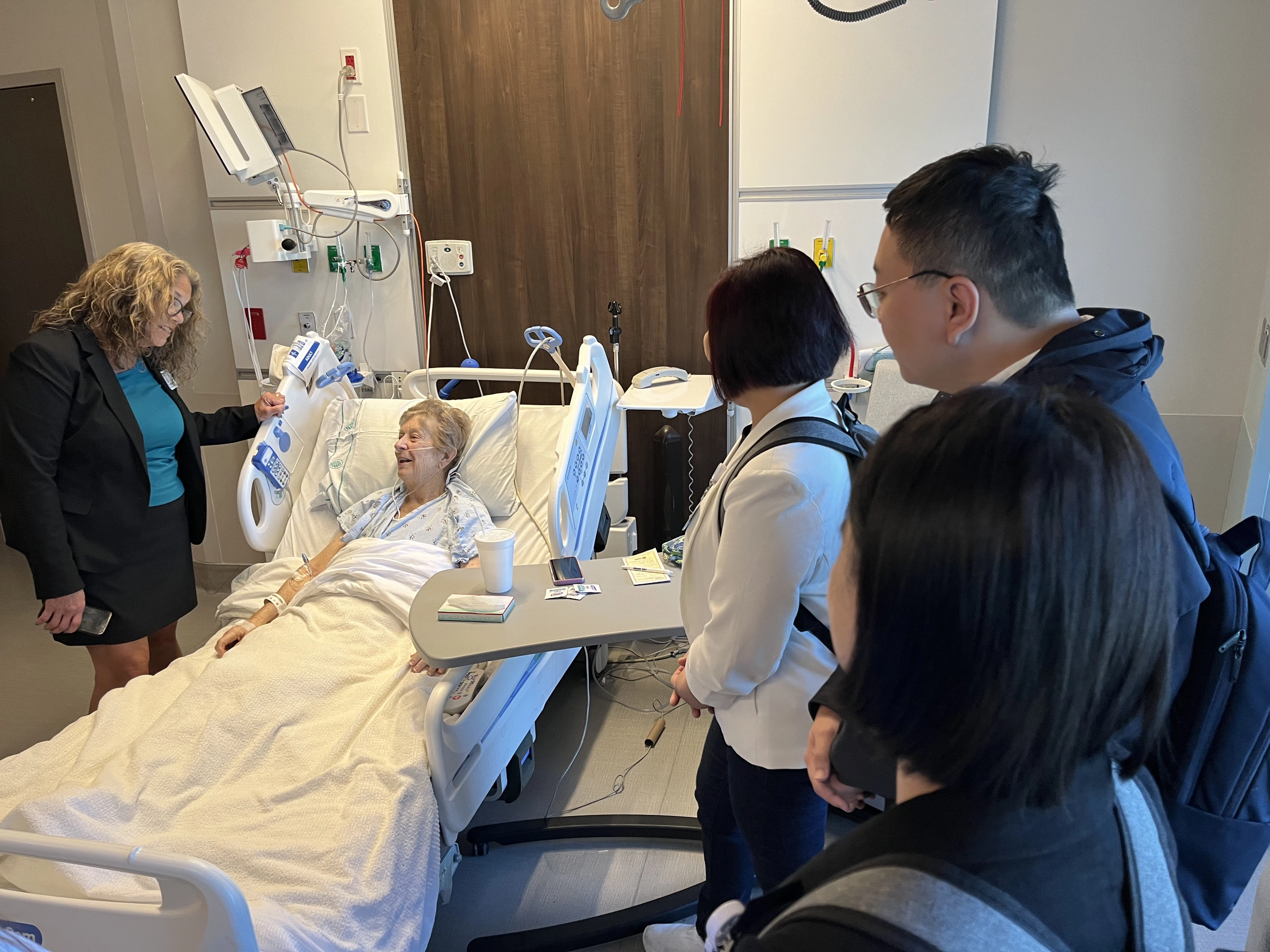 People in a hospital room with a patient in a bed