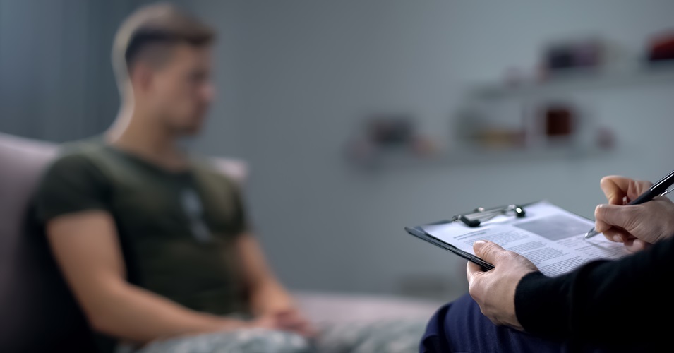 A person filling out paperwork on a clipboard, sitting across from another person.